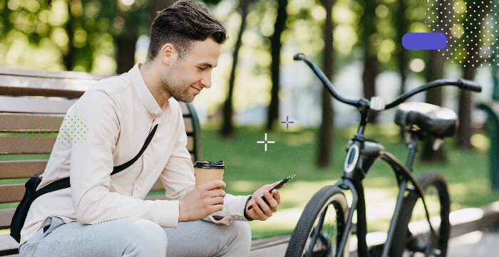 Young adult sitting in the park next to his bike checking his messages on his cell phone