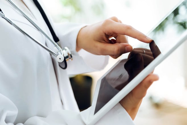 Hands of a doctor interacting with a tablet, stethoscope, white coat