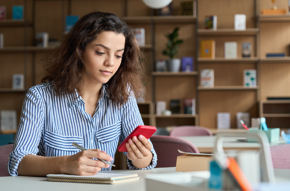 chica ve su teléfono mientras estudia en una biblioteca