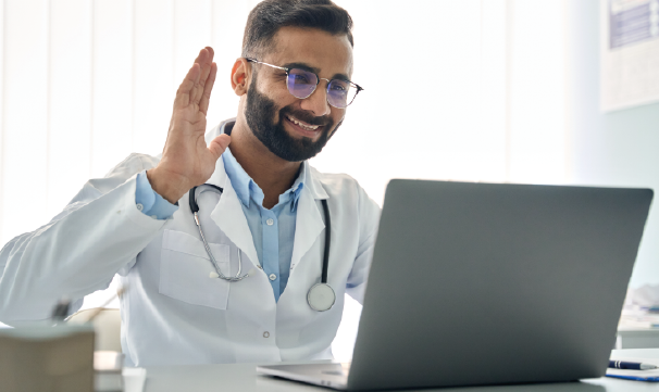 Doctor de sexo masculino con barba y anteojos saluda a una computadora portátil