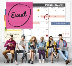 De fondo un calendario con la palabra evento resaltada y delante seis personas sentadas revisando sus dispositivos