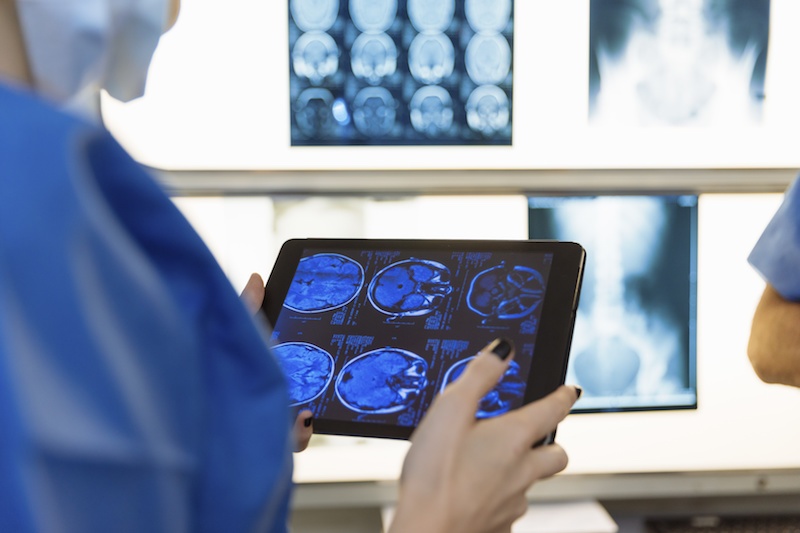 Doctora revisando radiografías en la pantalla de un ipad y en una pizarra iluminada de fondo