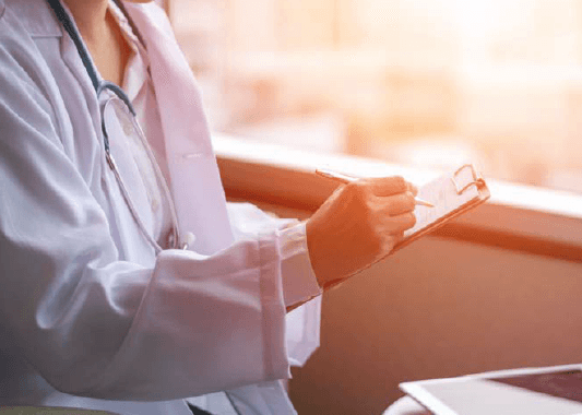 Doctora anotando en una tableta cerca de una ventana - ACF