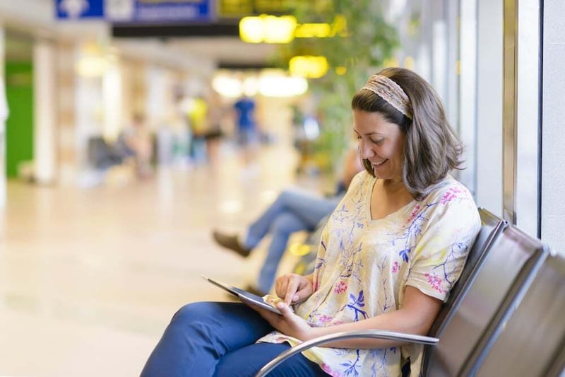 Mujer sentada en las sillas de un aeropuerto revisando su ipad portátil