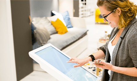 Mujer de pelo corto, con lentes y chaqueta gris revisando dos pantallas de aparatos electrónicos