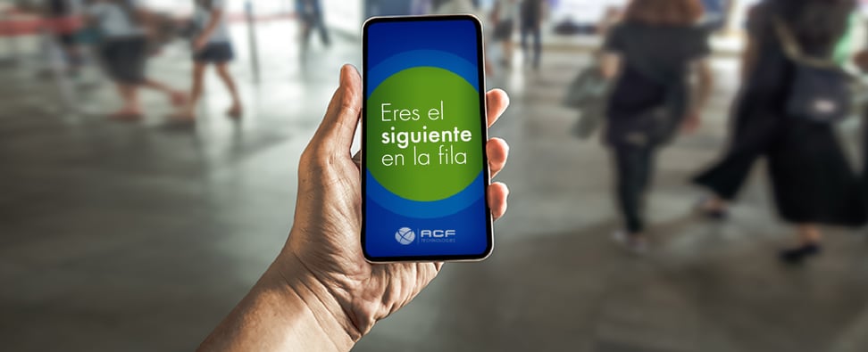 Mano izquierda sosteniendo un smartphone y en la pantalla se lee Eres el siguiente en la fila