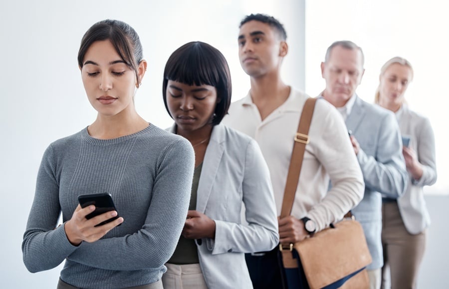 Clientes esperando en una fila, con una persona consultando su teléfono móvil.
