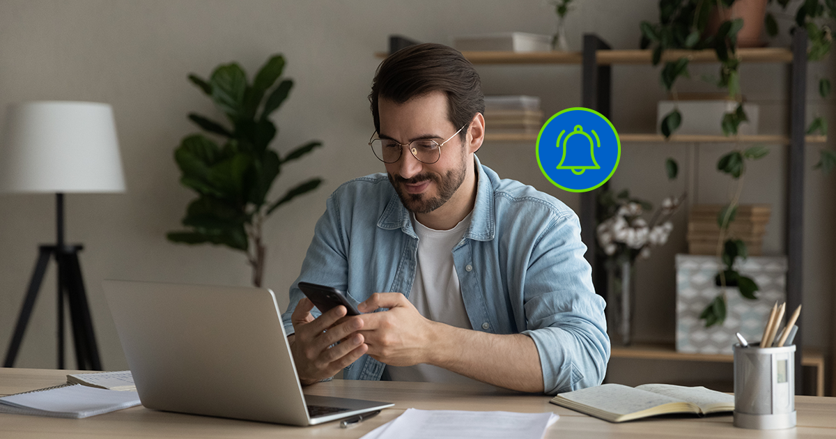 Homem sentado em sua mesa revisando uma notificação que veio a ele em seu smartphone