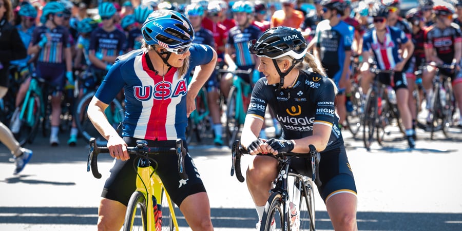 Pair of cyclists talking with one of them wearing Wiggle-branded clothes