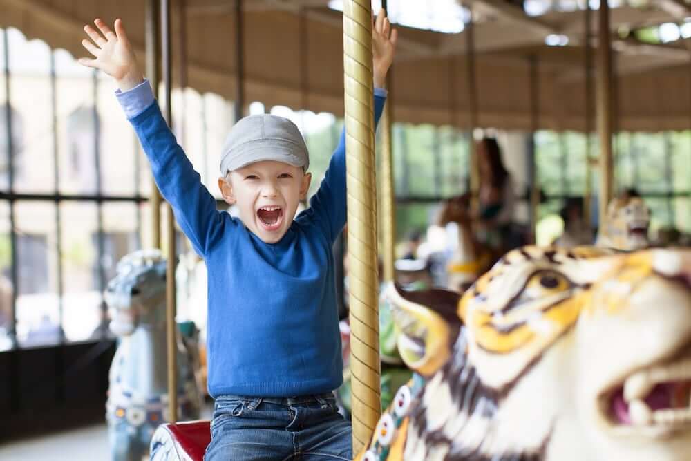 Boy on carousel, riding a tiger and raising his hands