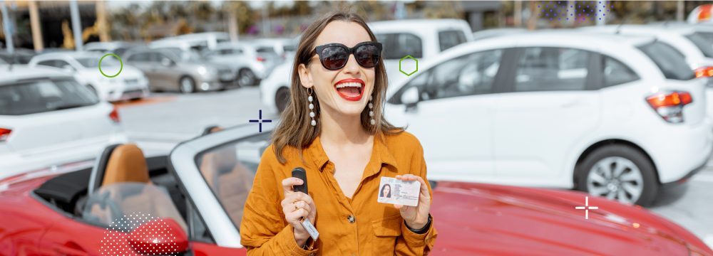 Woman smiling while showing her driver's license in one hand and keys in the other hand, with a red car in the background.