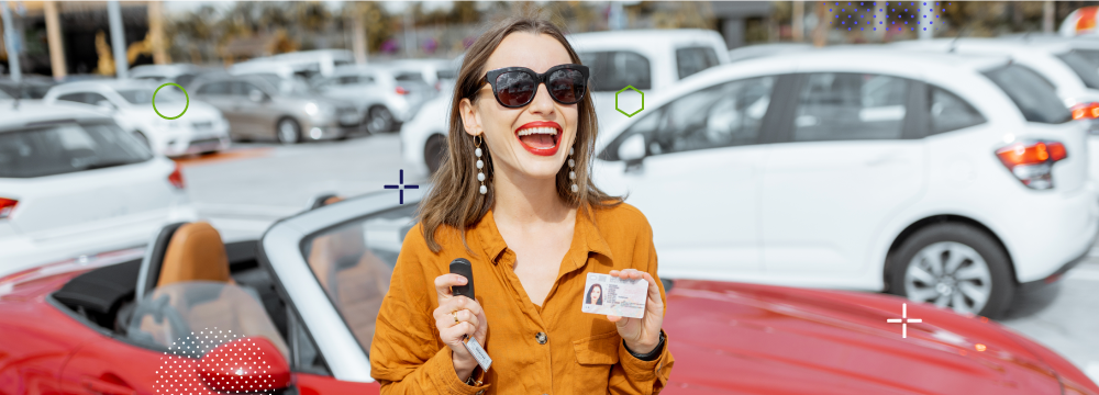 Mujer sonriendo mientras muestra su licencia de conducir con un auto rojo al fondo.