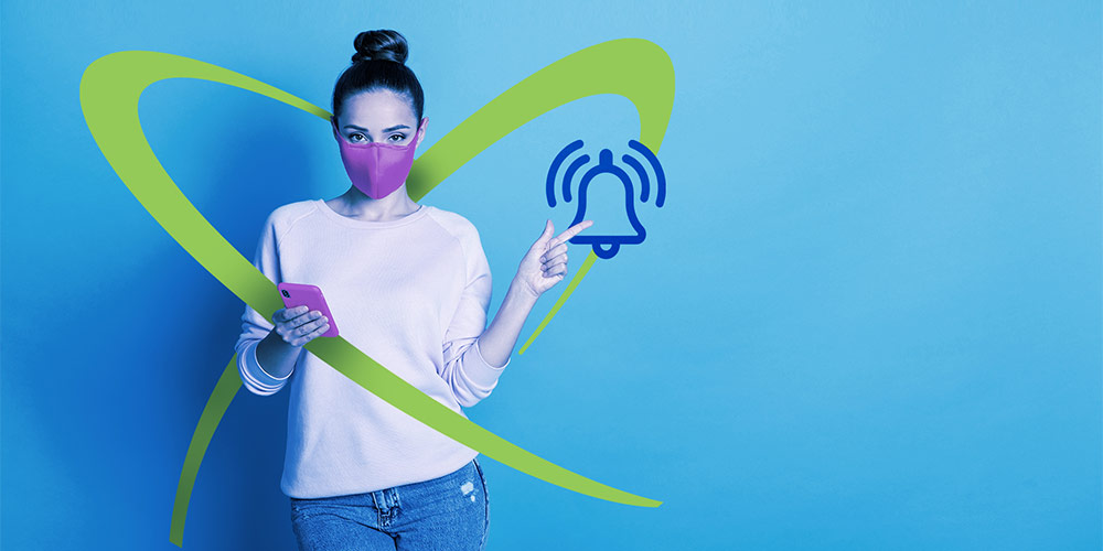 Uma mulher usando uma máscara com seu smartphone em uma mão e a outra apontando para um ícone de sino acima do logotipo da ACF Technologies