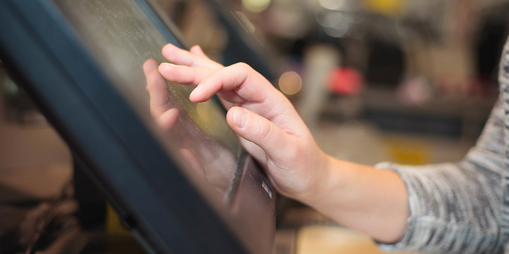 A mão de uma mulher tocando uma tela sensível ao toque dentro de uma loja