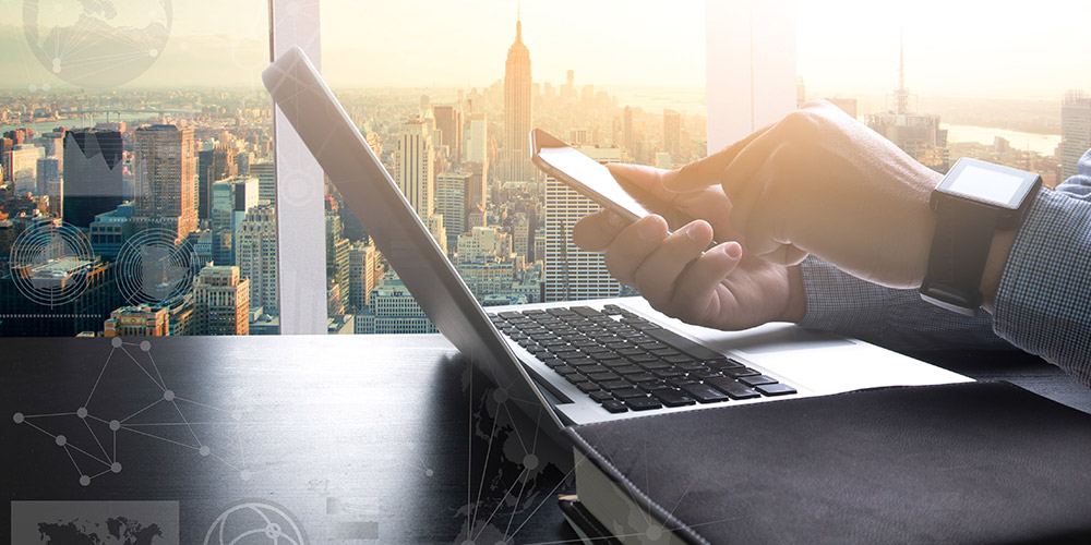 Detalhe foco em algumas mãos com um smartphone e um laptop na mesa com uma cidade atrás ao pôr do sol.