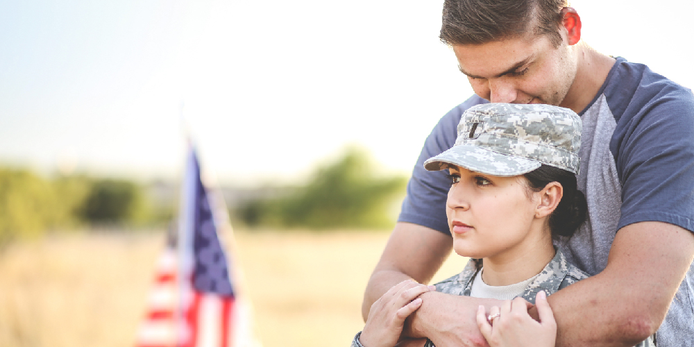 US Military veteran and partner in field with flag.