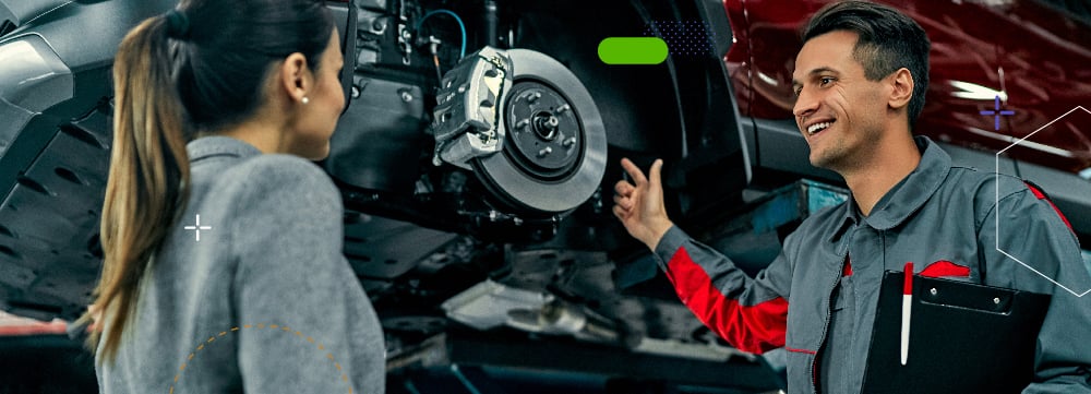 Male mechanic at a service center showing a female client her car being fixed.