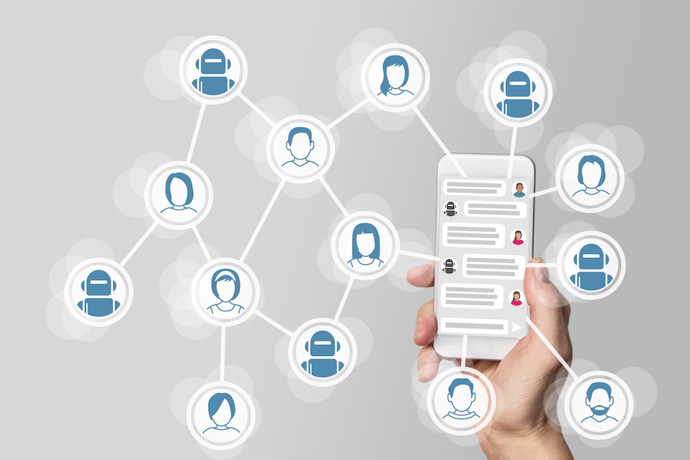 Imagem de uma mão segurando um smartphone com vários ícones de pessoas e alguns robôs formando uma rede fora do telefone