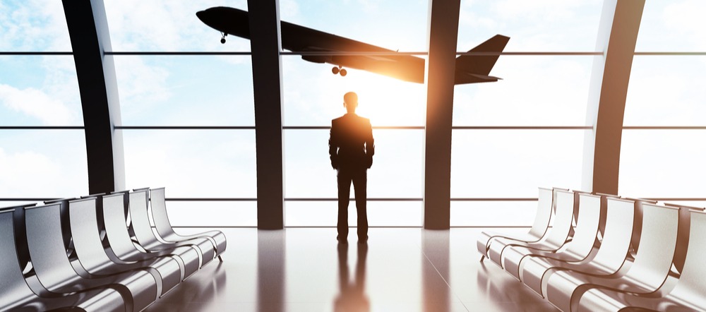 Hombre en el aeropuerto frente a una ventana donde se ve un avión despegando