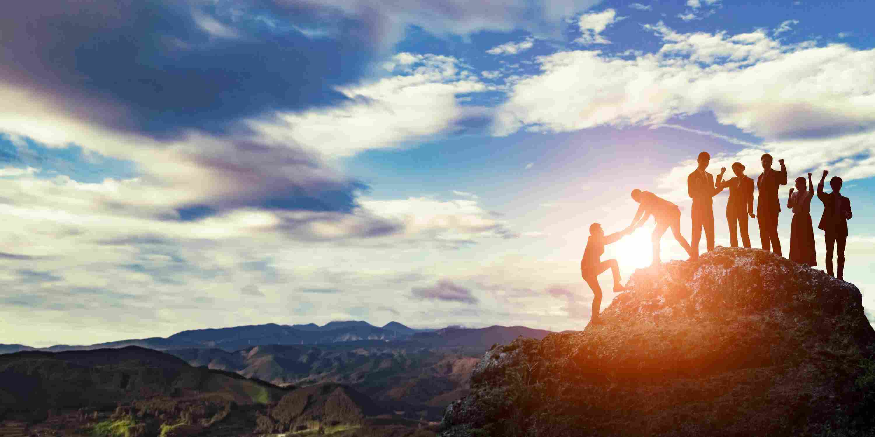 Group of people hiking a mountain, helping each other to get to the top