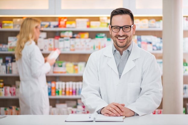 Dependiente de farmacias con medicamento en mano asesorando a cliente 