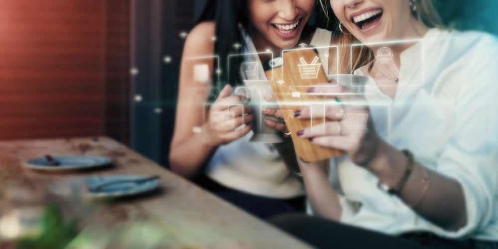 Two women enjoy shopping while waiting at a restaurant. 