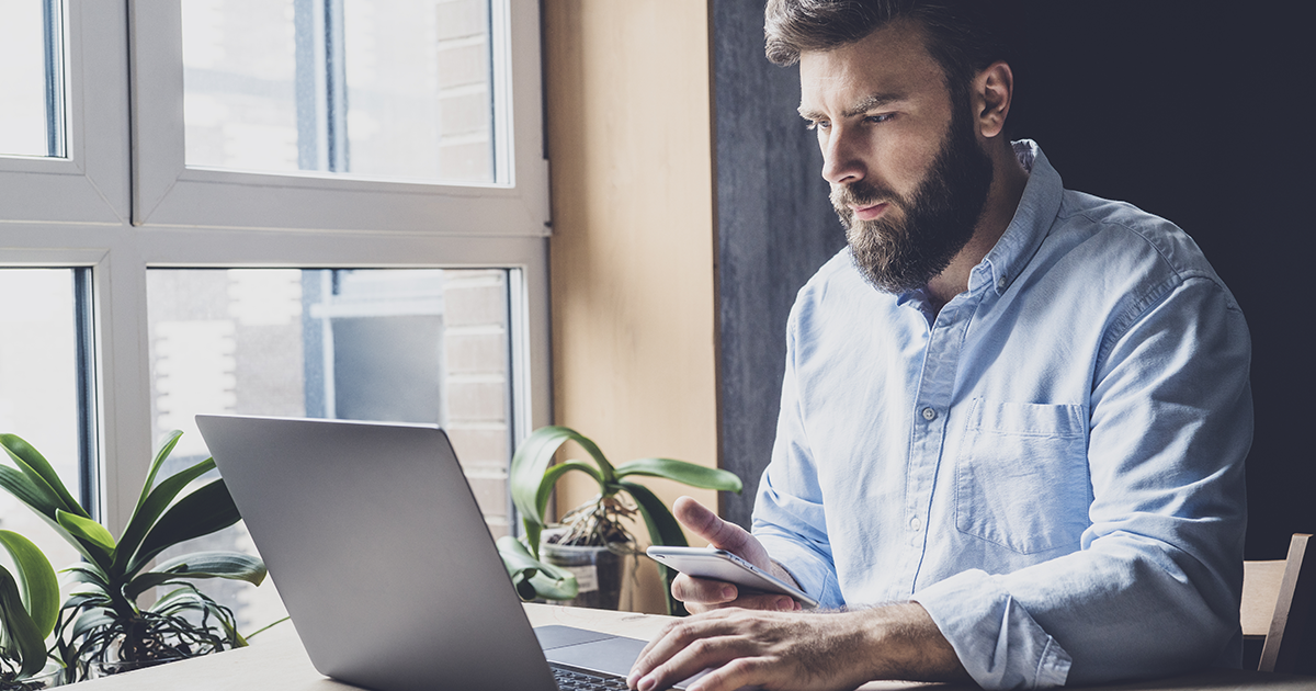 Hombre frente a computador con celular en su mano - ACF