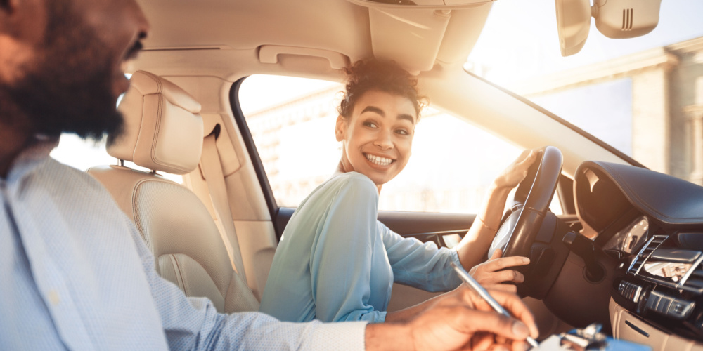 Mujer conduciendo feliz con persona a la par evaluandola
