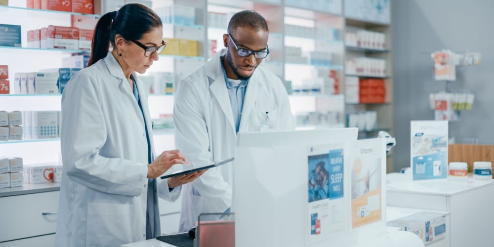 Two pharmacists use a tablet to check medication status. 